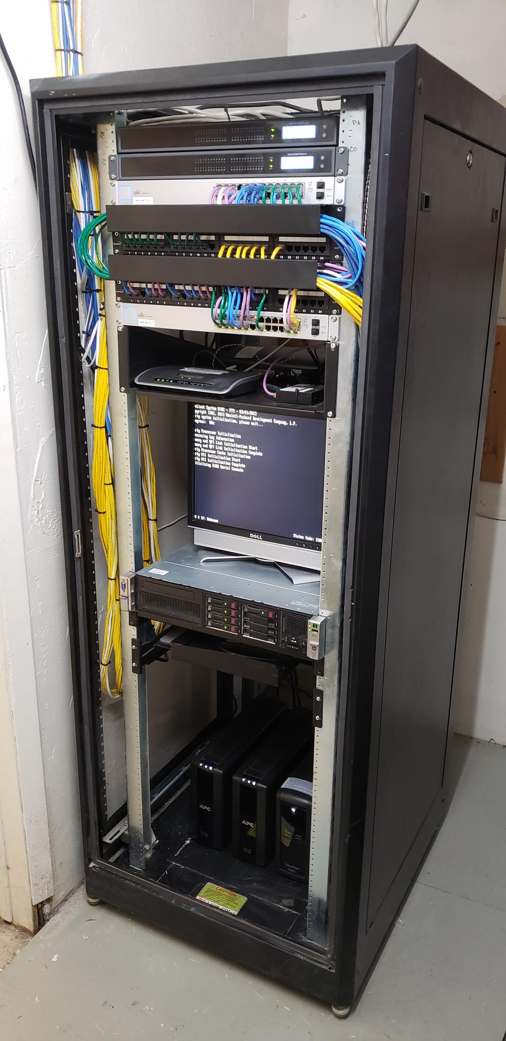 Rebuilt rack at handover: voice gateways and switches above patch panels, server below, UPS bank at the base